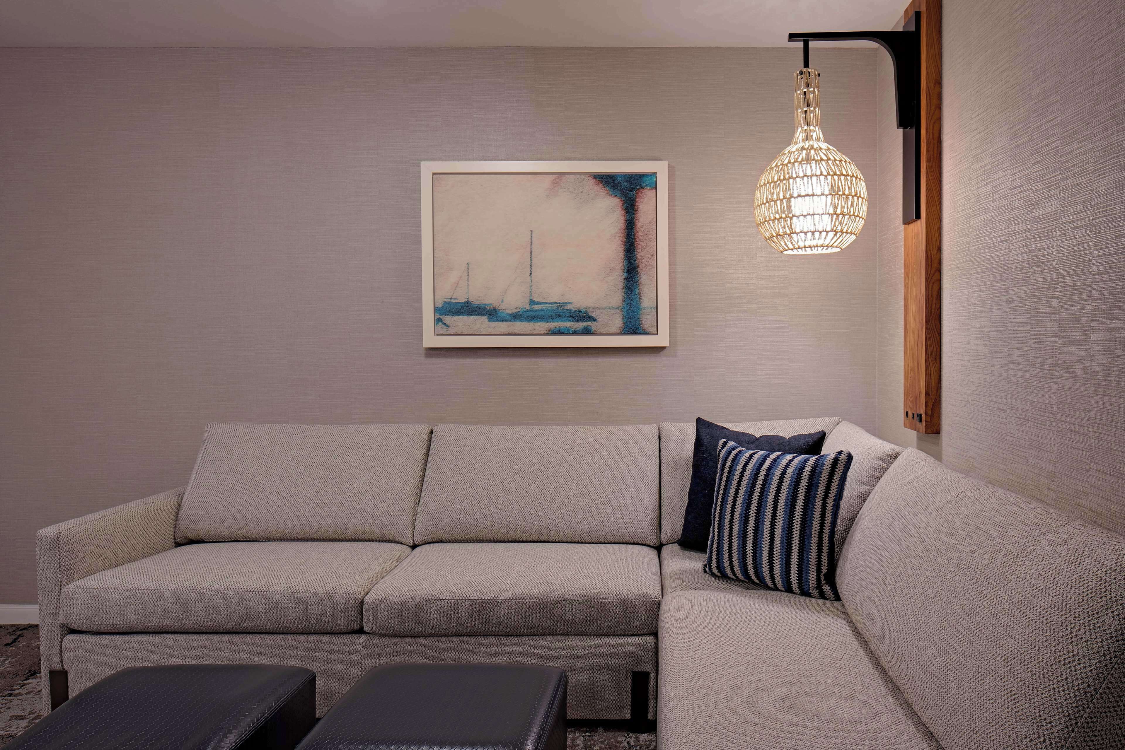 A modern living room with a beige sofa, a framed abstract painting, and a hanging light fixture.