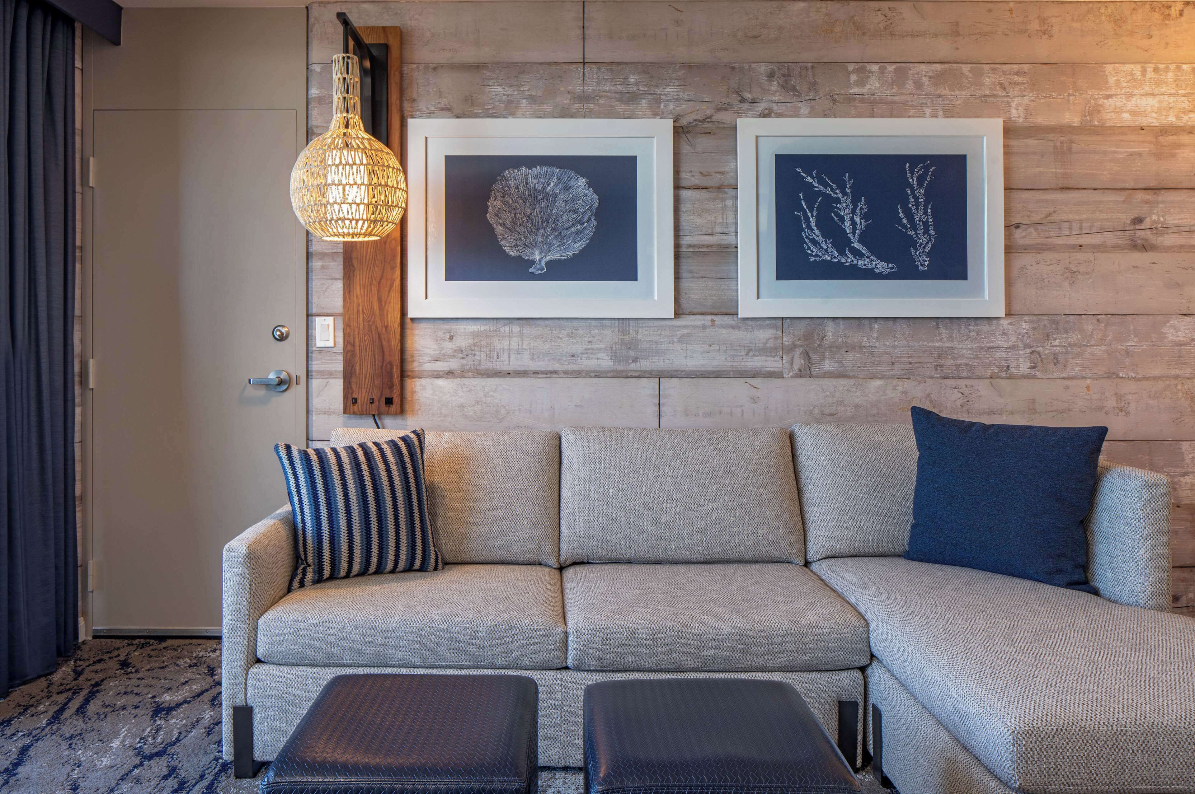 A modern living room with a sofa, two framed artworks, a hanging light fixture, and a wooden wall.