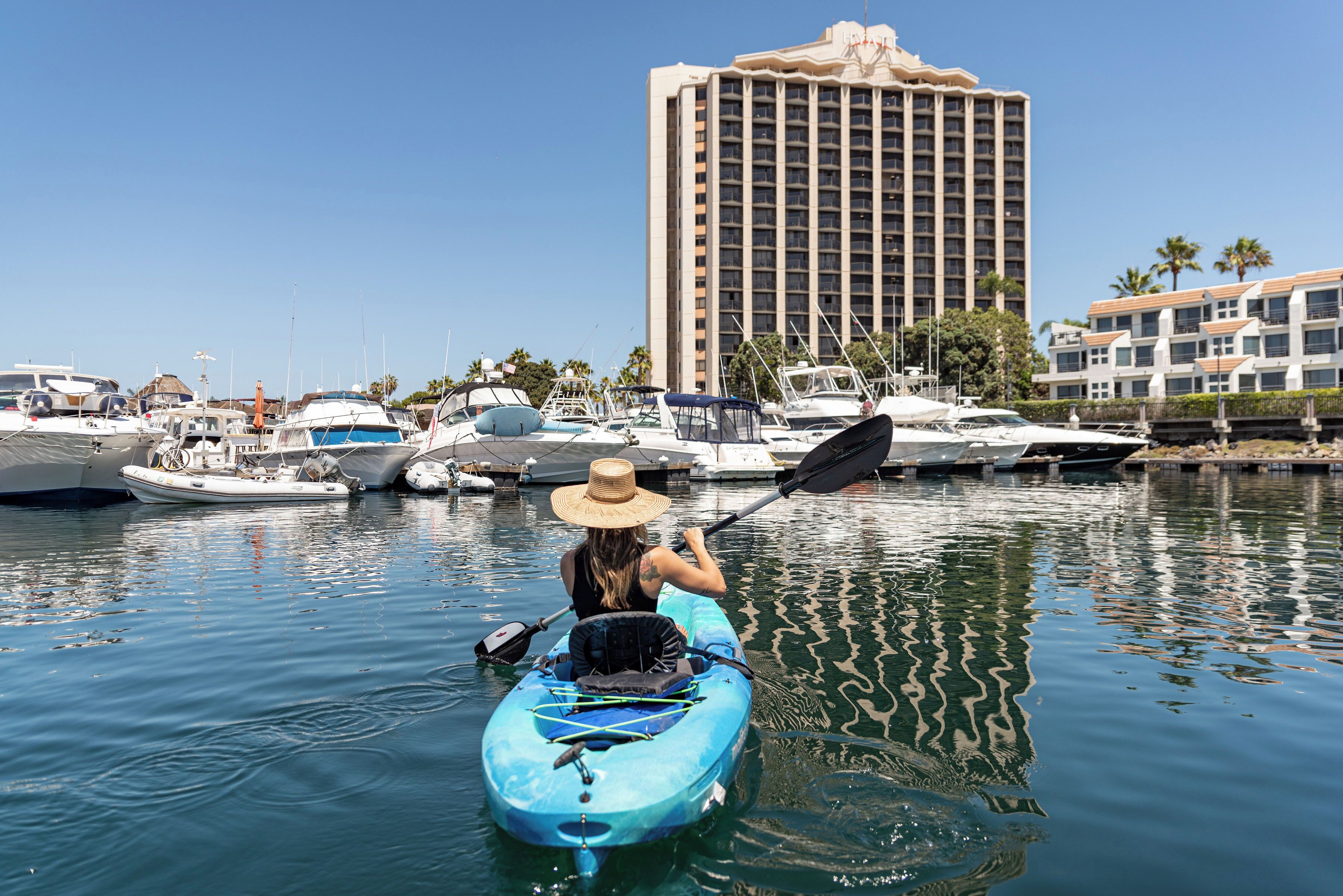 A person kayaking on a body of water with a marina and a hotel in the background.