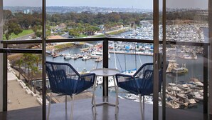 Un balcón con dos sillas y una pequeña mesa, con vistas a un puerto deportivo con numerosos barcos y un paisaje urbano al fondo.