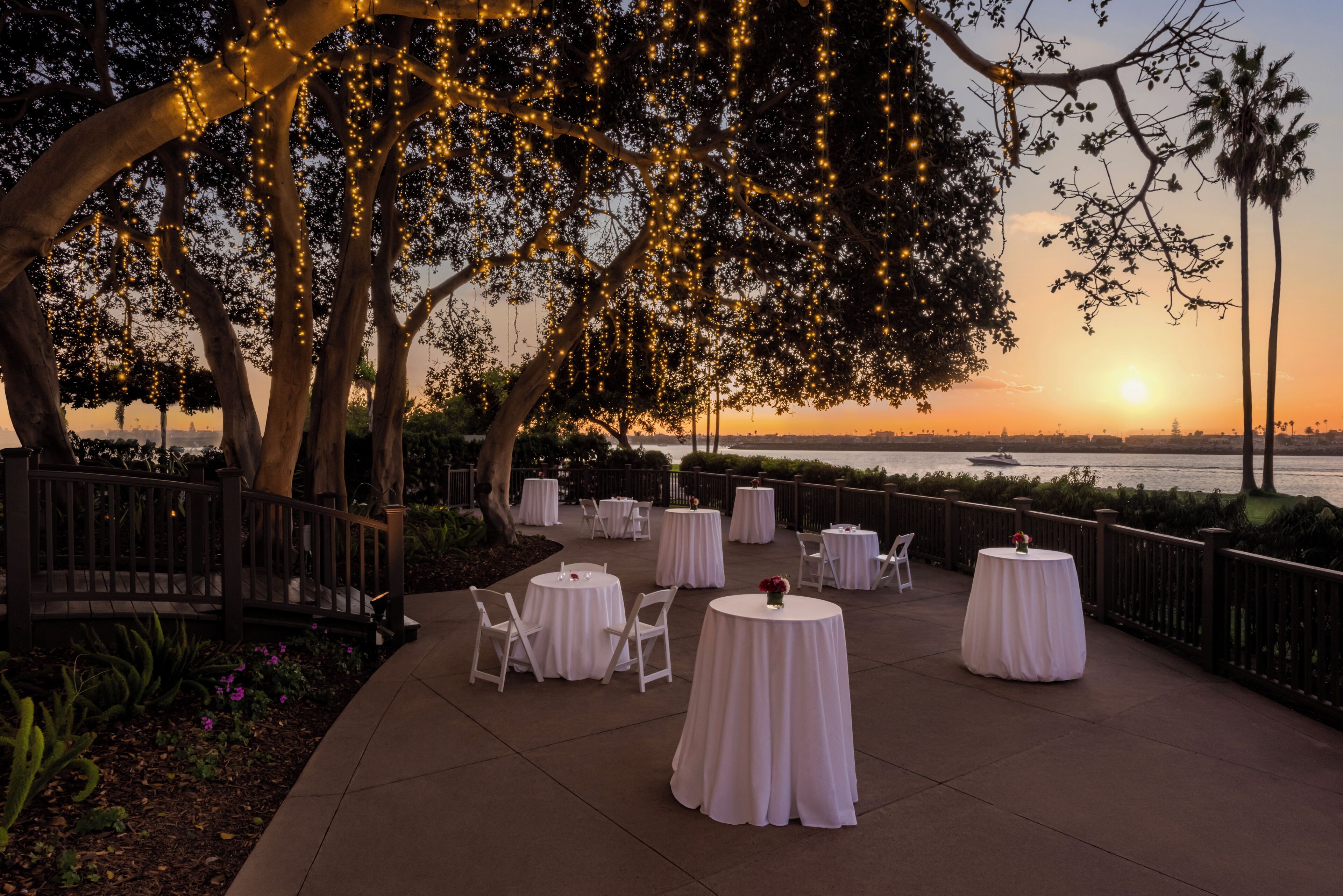 An outdoor seating area with round tables and chairs, overlooking a body of water.