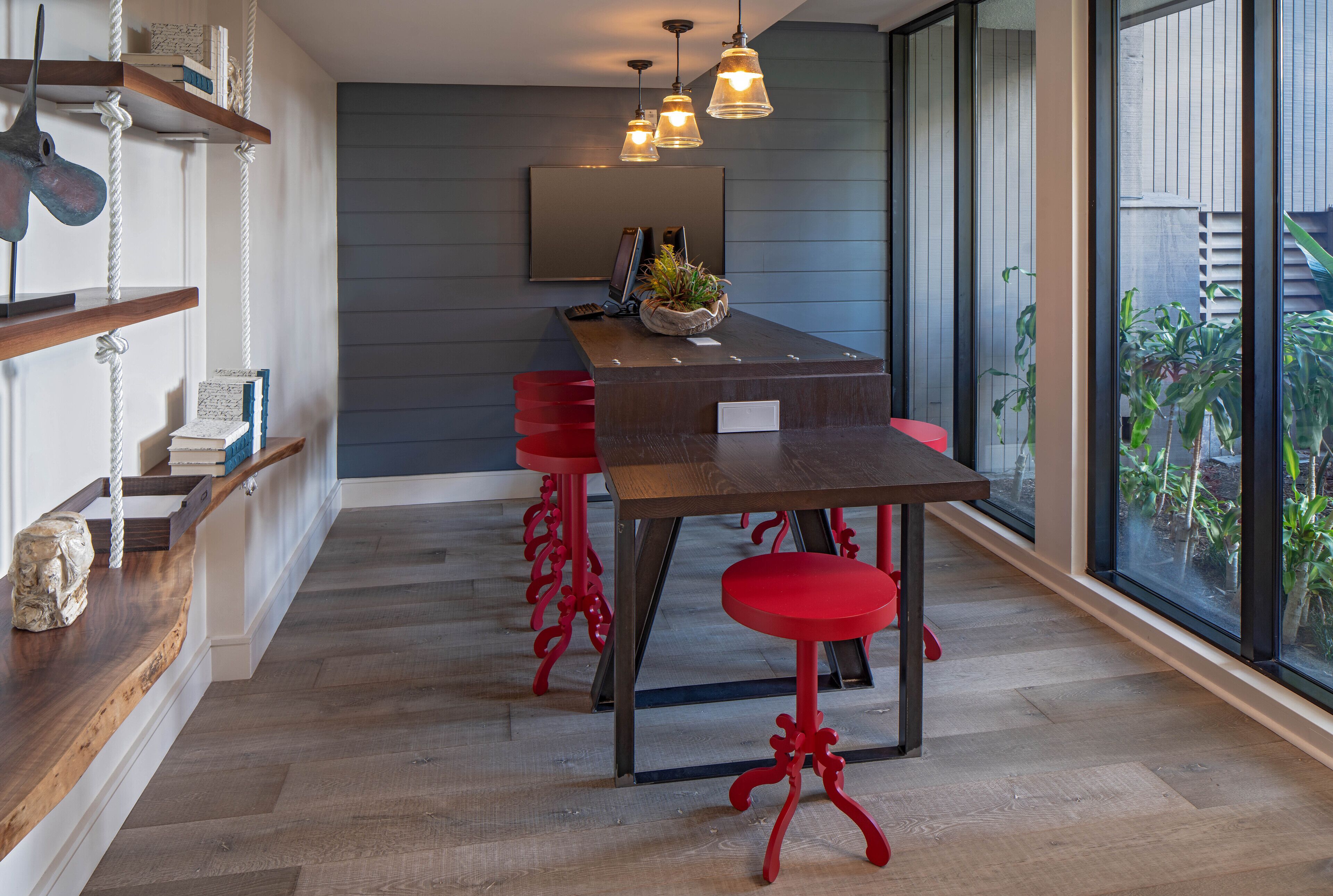 A modern kitchen with a wooden table, red bar stools, and pendant lighting.