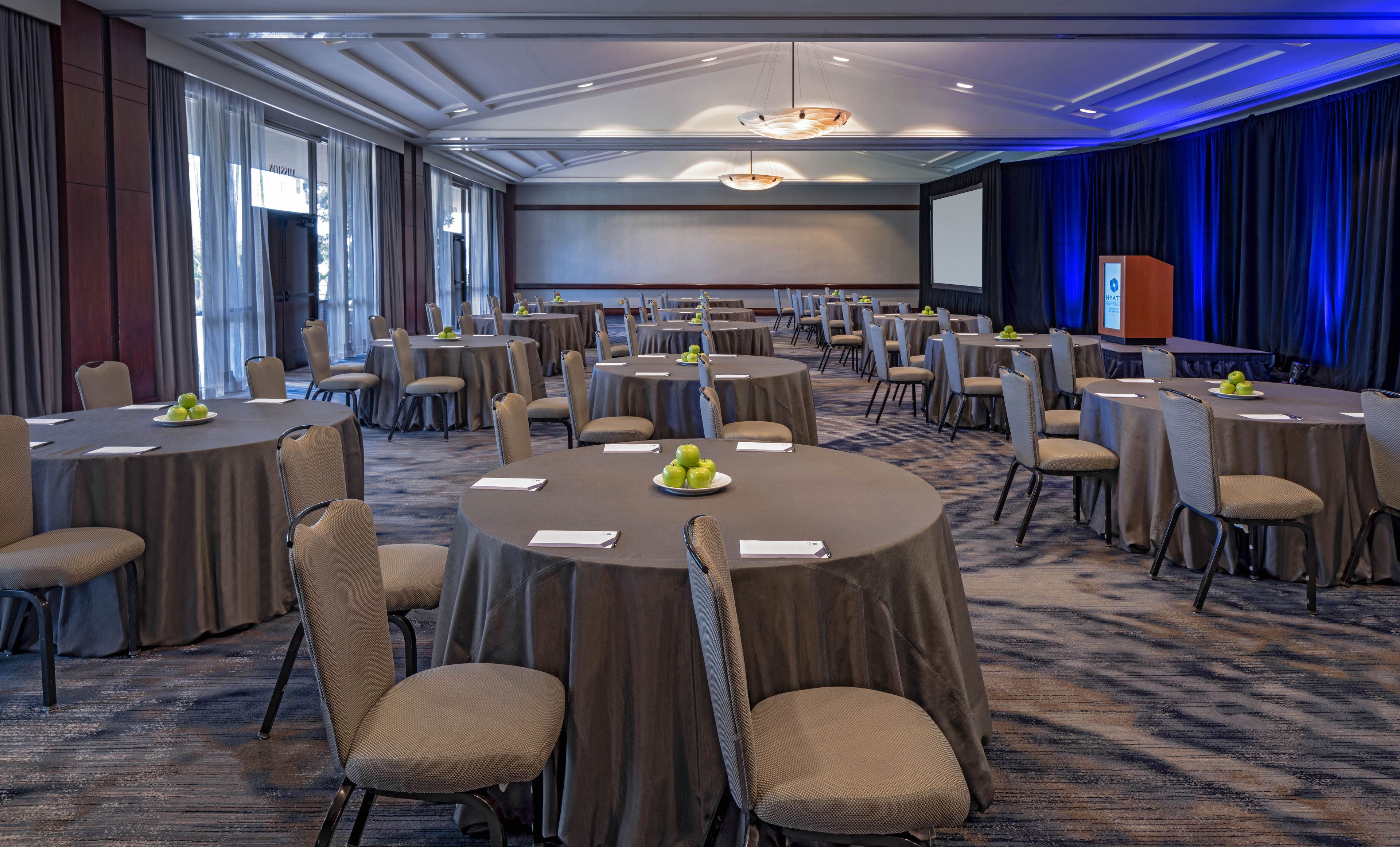 A conference room with round tables, chairs, and a projector screen.