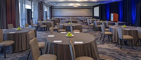 A conference room with round tables, chairs, and a projector screen.