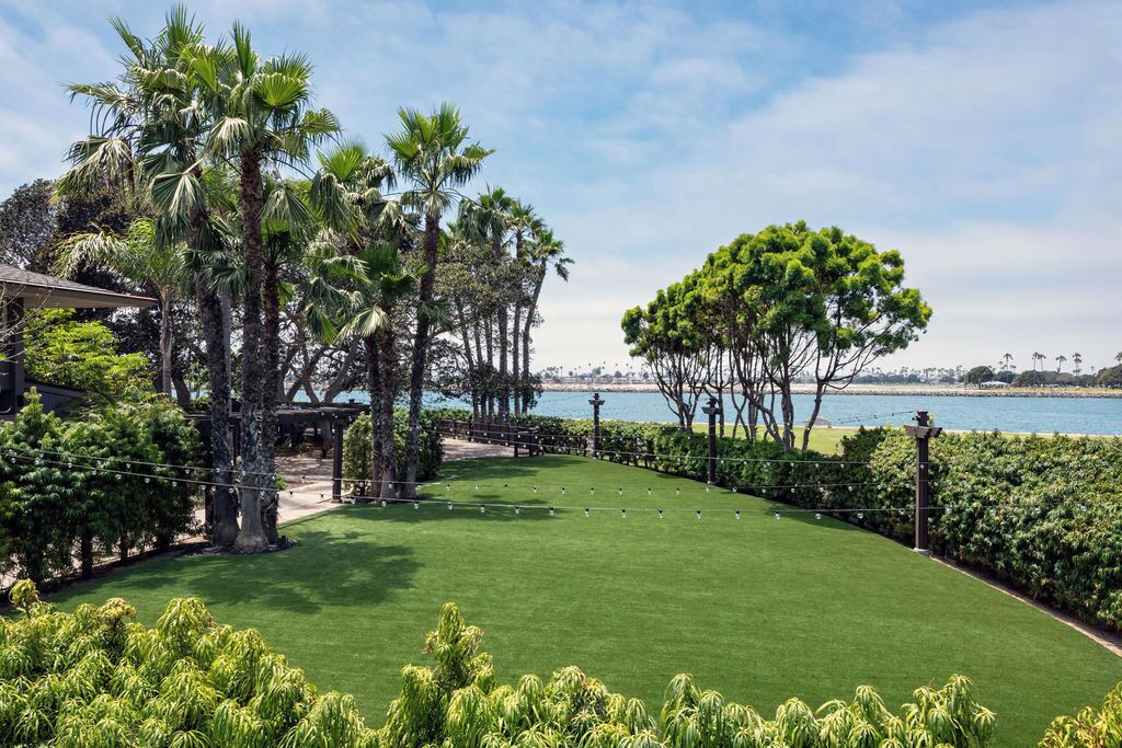 A well-maintained lawn with a gazebo, palm trees, and a view of the water.
