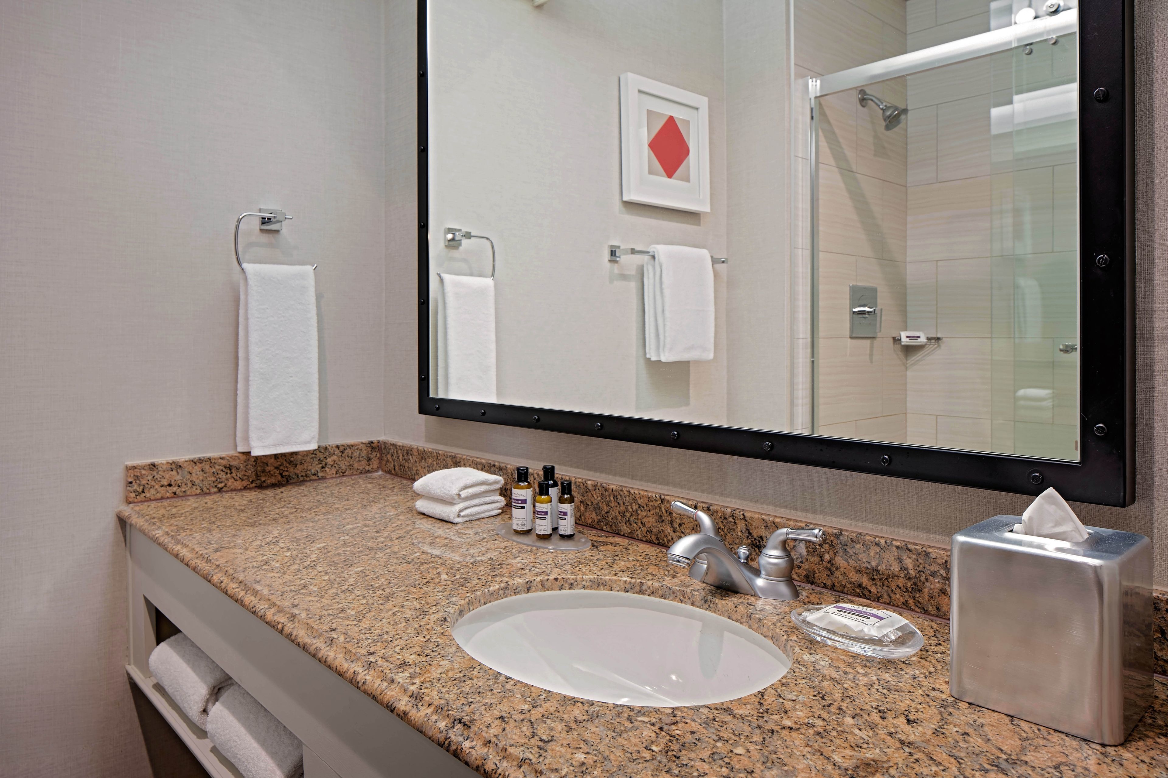Une salle de bain avec un comptoir en granit, un lavabo, un miroir et un porte-serviettes.
