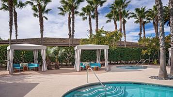 A pool area with two covered seating areas, palm trees, and a clear sky.