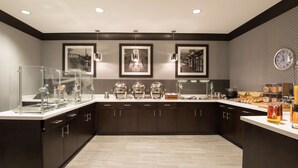 A modern kitchen with dark cabinetry, a central island with a glass enclosure, and overhead pendant lighting. - DoubleTree by Hilton Schenectady Downtown (Schenectady)