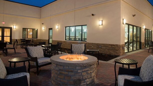 An outdoor patio area with stone fire pit seating, tables, and chairs, surrounded by a building with large windows and exterior lighting. - DoubleTree by Hilton Schenectady Downtown (Schenectady)