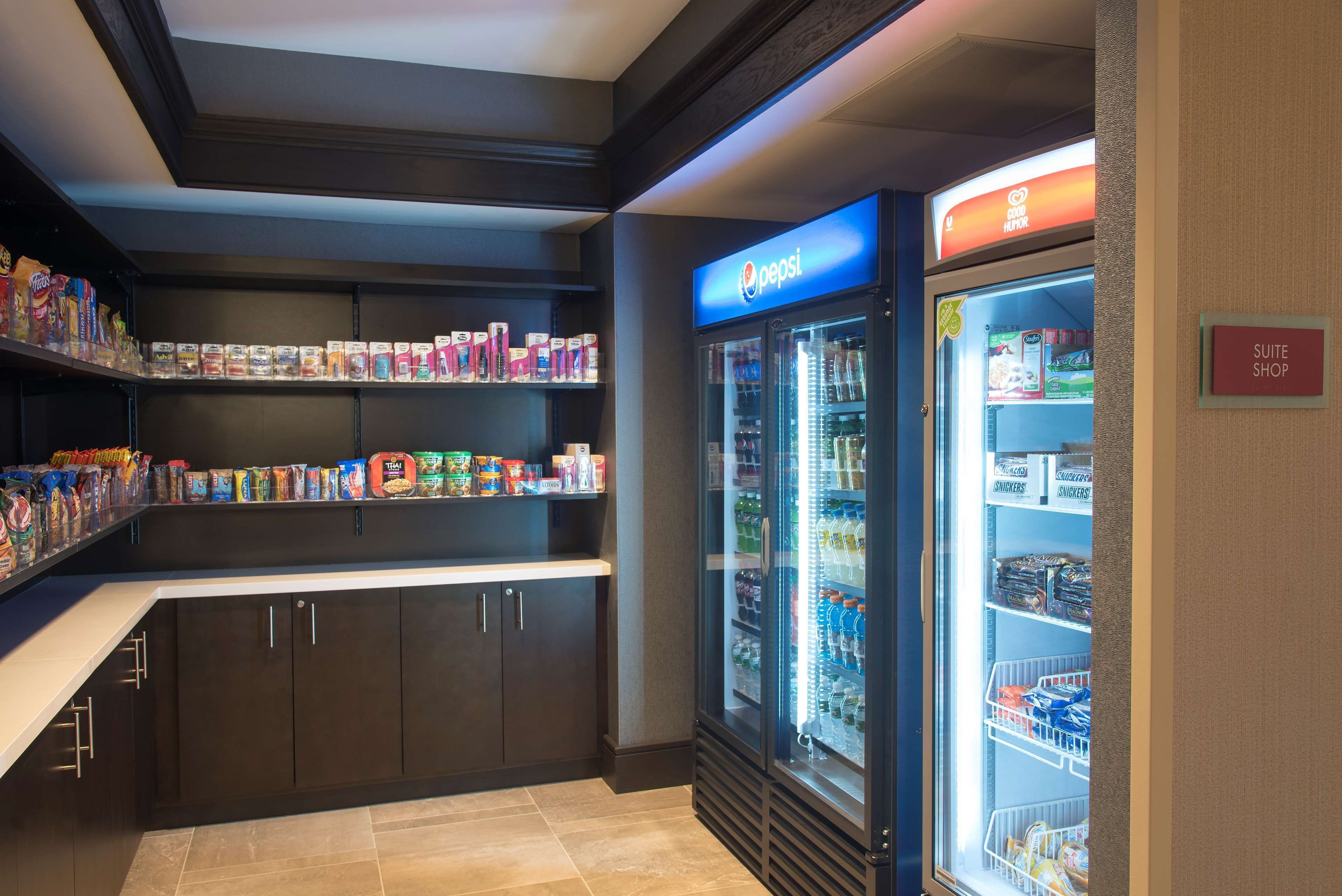 Un angolo cottura con frigorifero Pepsi, ripiani per snack e insegna dello shop della suite.