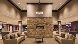 A lobby with a stone wall, two sofas, a coffee table, and a chandelier. - DoubleTree by Hilton Schenectady Downtown (Schenectady)