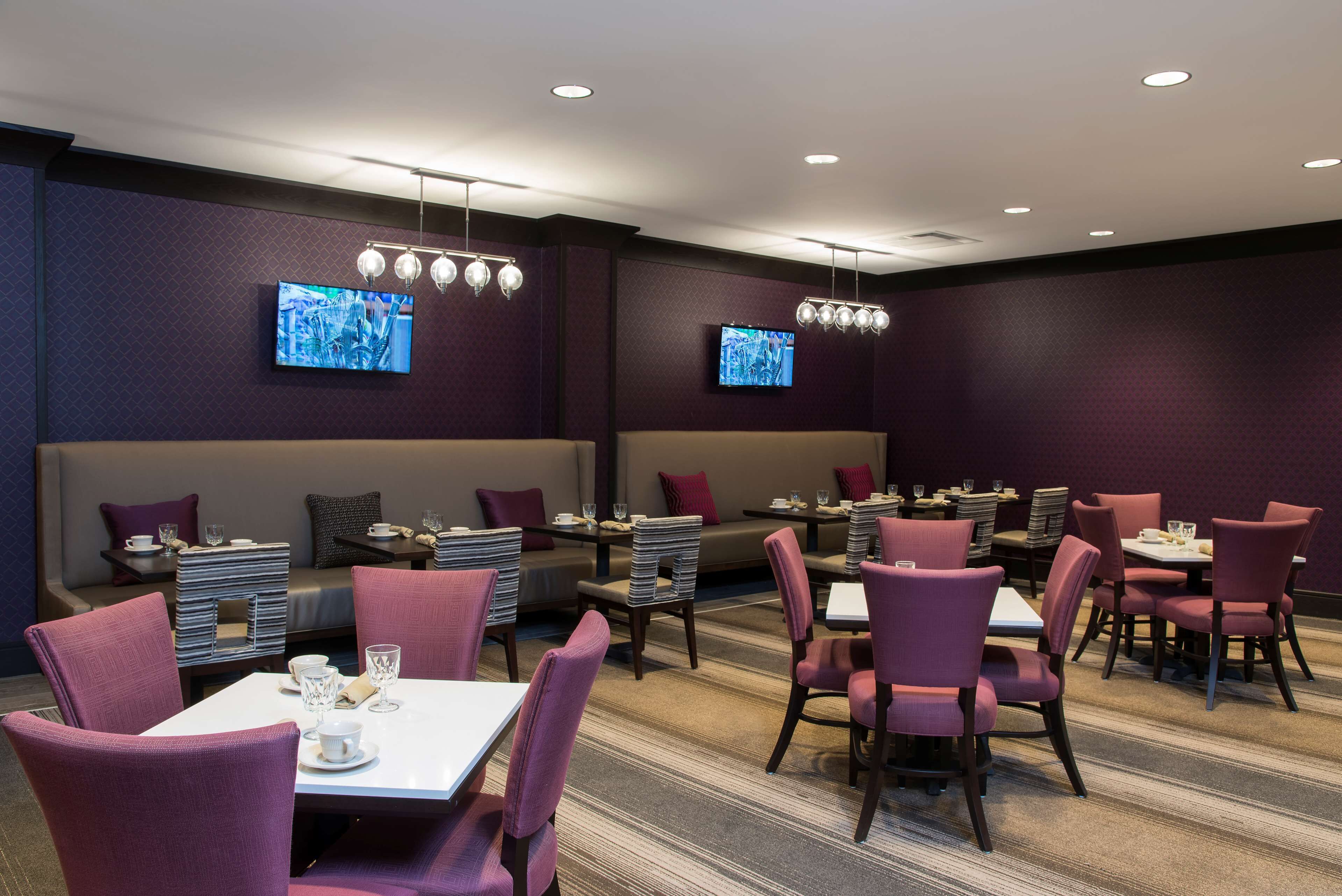 A modern dining area with purple upholstered chairs, white tables, and recessed lighting.