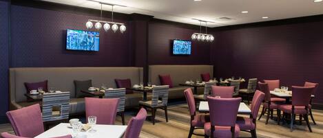 A modern dining area with purple upholstered chairs, white tables, and recessed lighting.