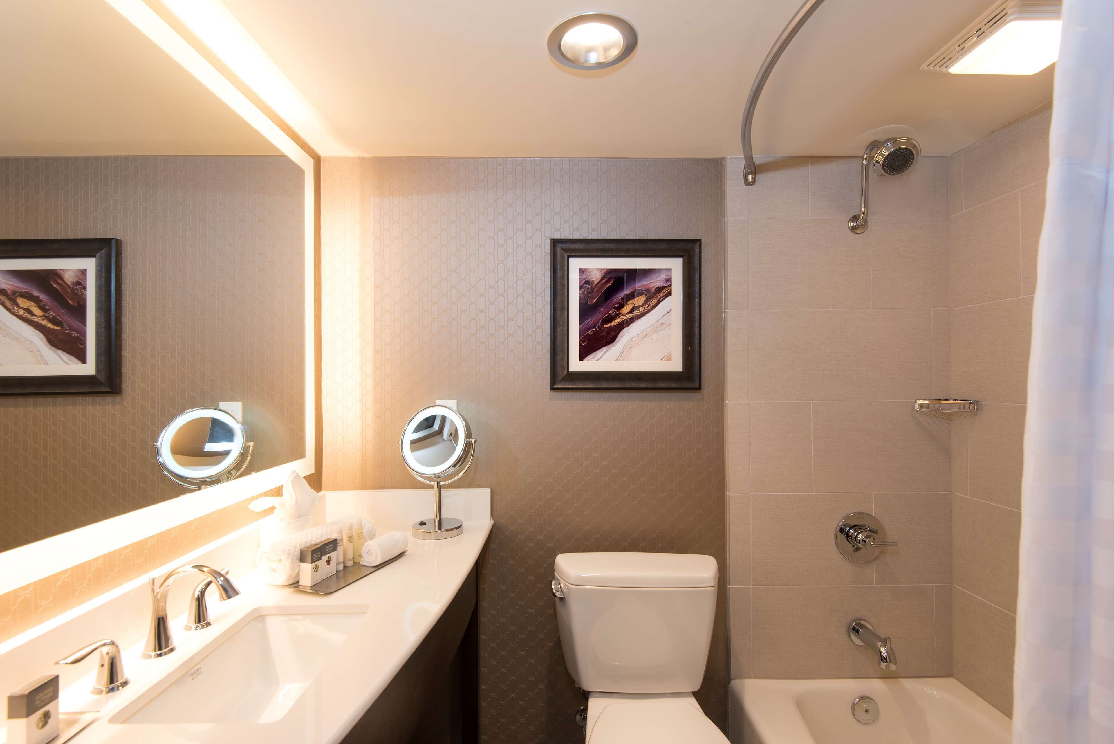 Et moderne badeværelse med vask, to spejle, toilet og brusebad.