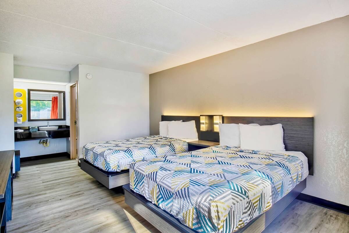 A modern hotel room with two beds, a bathroom, and a small sitting area.