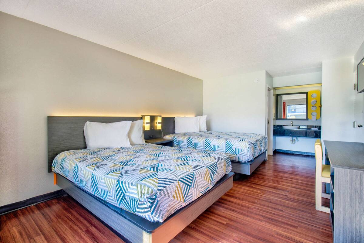 A hotel room with two beds, a small kitchenette, and a wooden floor.