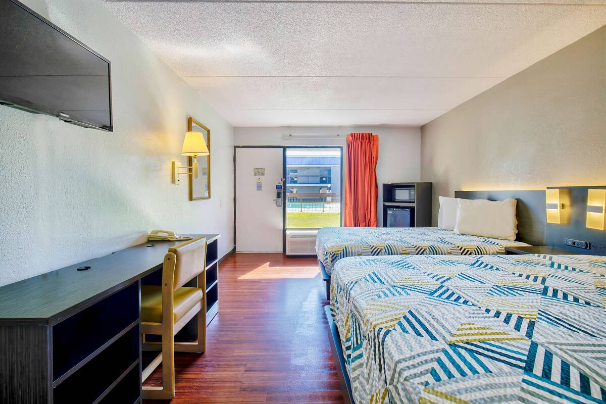 A hotel room with a bed, a desk, a chair, a TV, and a window with curtains.