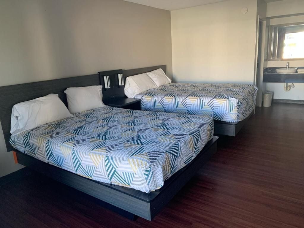 A hotel room with two beds, a nightstand, a small table, and a bathroom visible through an open door.