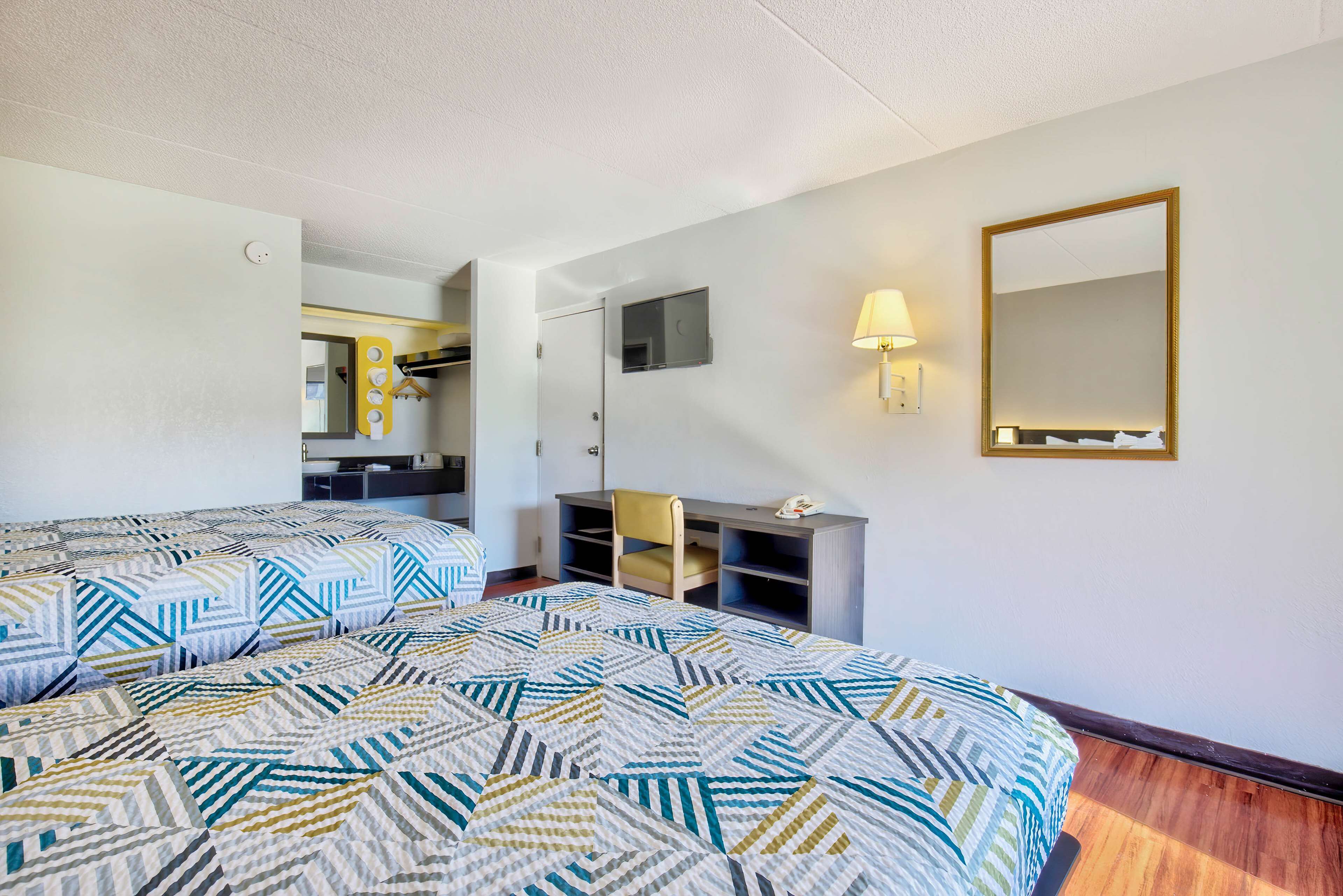 A hotel room with two beds, a desk, a chair, a TV, and a mirror.