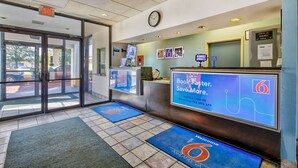 A hotel reception area with a digital screen displaying a welcome message, a clock, and a photo ID check-in sign. - Motel 6 Ashland, VA (Ashland)