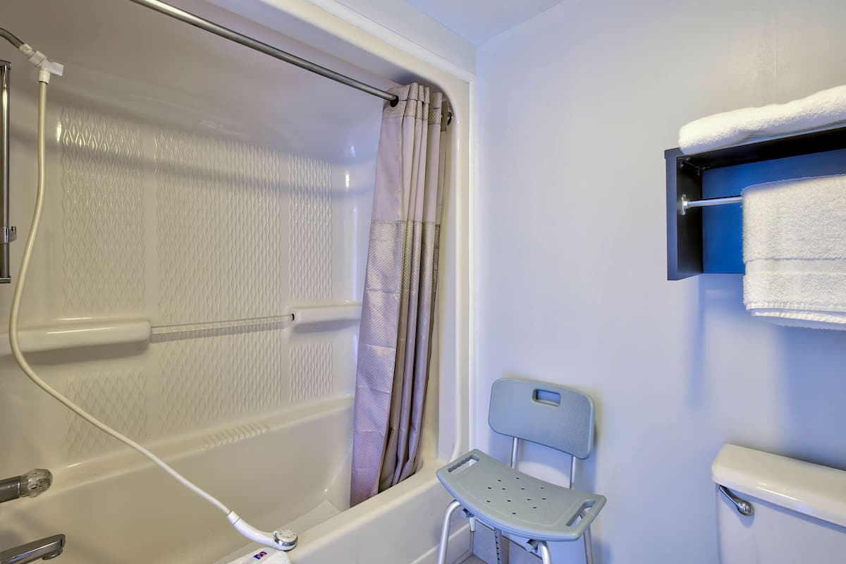 A bathroom with a bathtub, shower curtain, towel rack, and a small chair.