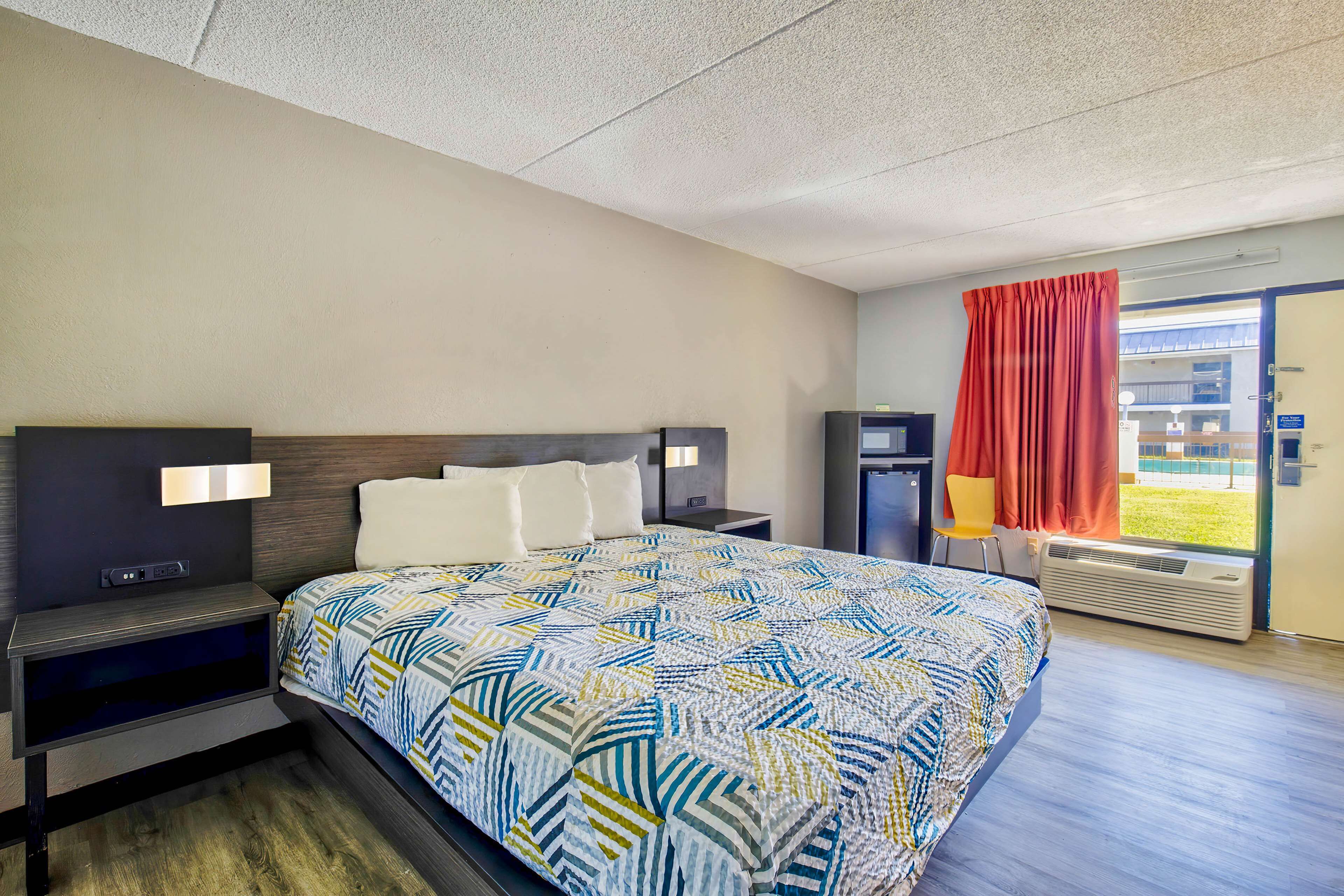 Camera d'albergo con un letto grande, televisore, scrivania e finestra con tende.