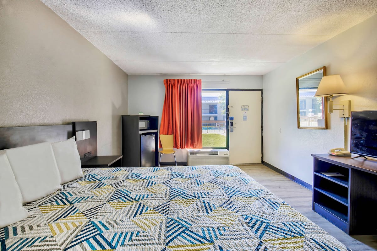A hotel room with a large bed, a desk, a TV, and a window with curtains.