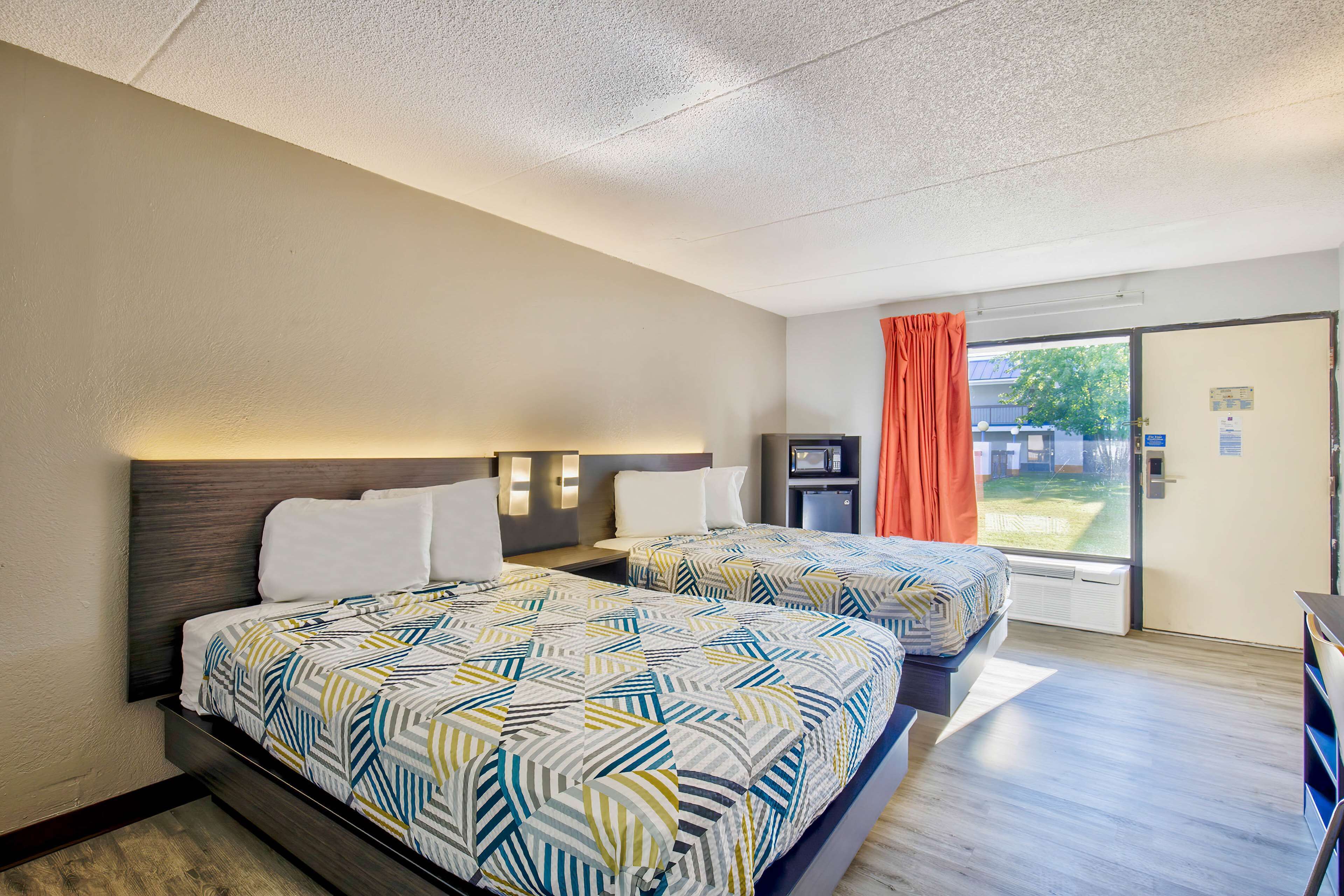 Habitación de hotel con dos camas, televisión, escritorio y ventana con cortinas.