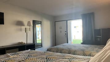 A hotel room with two beds, a desk, a lamp, and a view of the outside.