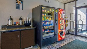 A vending machine with snacks and beverages, a coffee station, and a cart near a door. - Motel 6 Ashland, VA (Ashland)