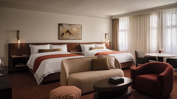 A hotel room with two beds, a sofa, a coffee table, and a dining table.