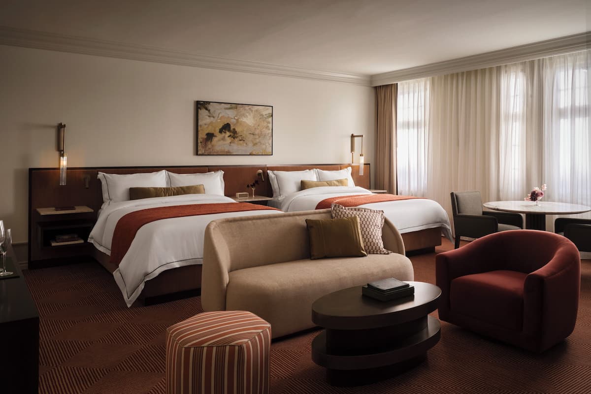 Habitación de hotel con dos camas, un sofá, una mesa de centro y una mesa de comedor.