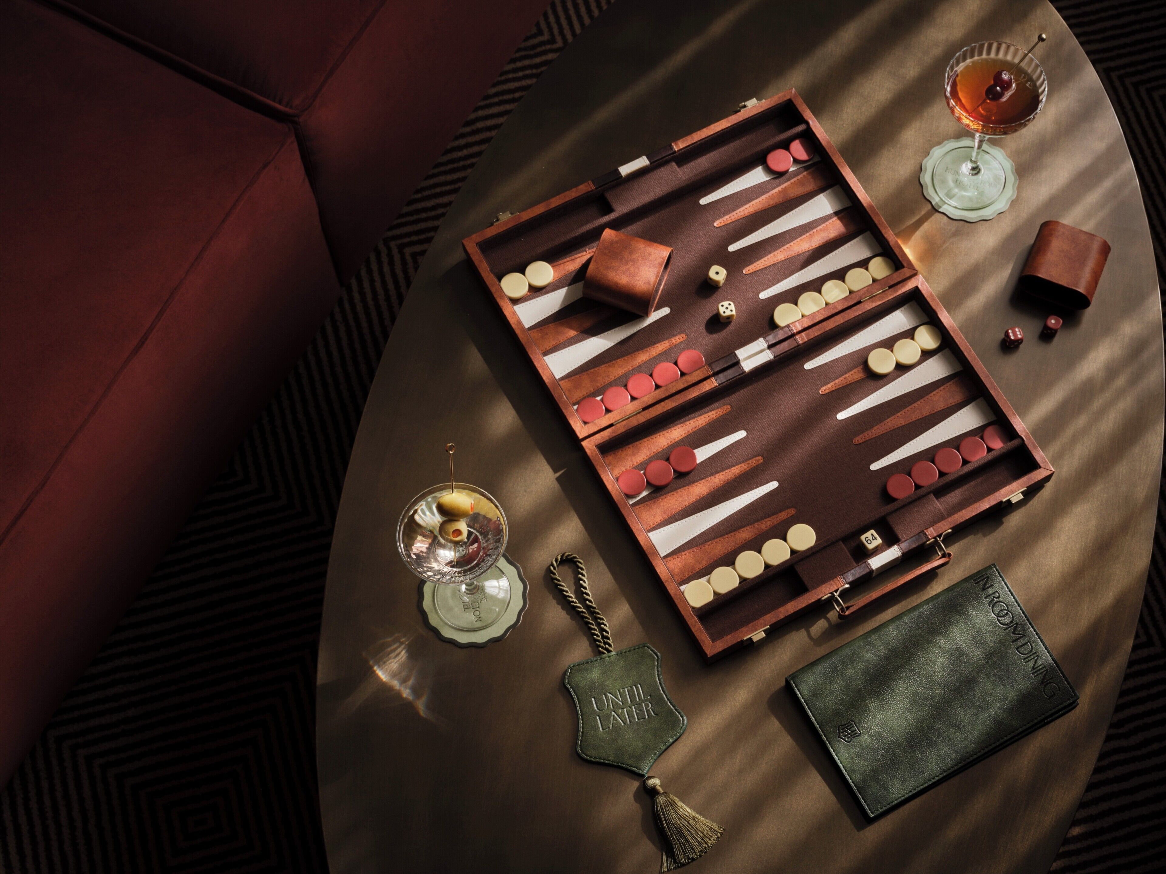 Una mesa de mahjong sobre una mesa de madera, con una billetera de cuero, una botella de licor y una pequeña caja.