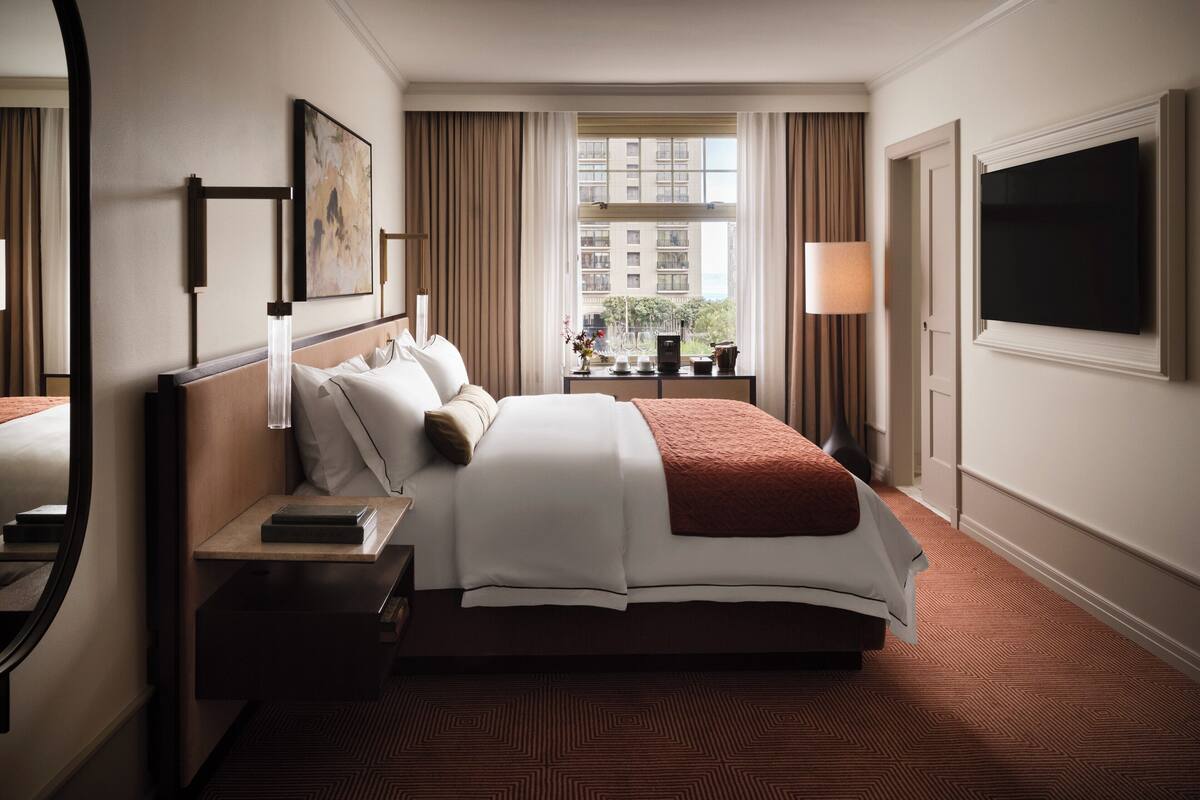 Habitación de hotel con una cama grande, una mesita de noche, una lámpara, un televisor y una ventana con cortinas.