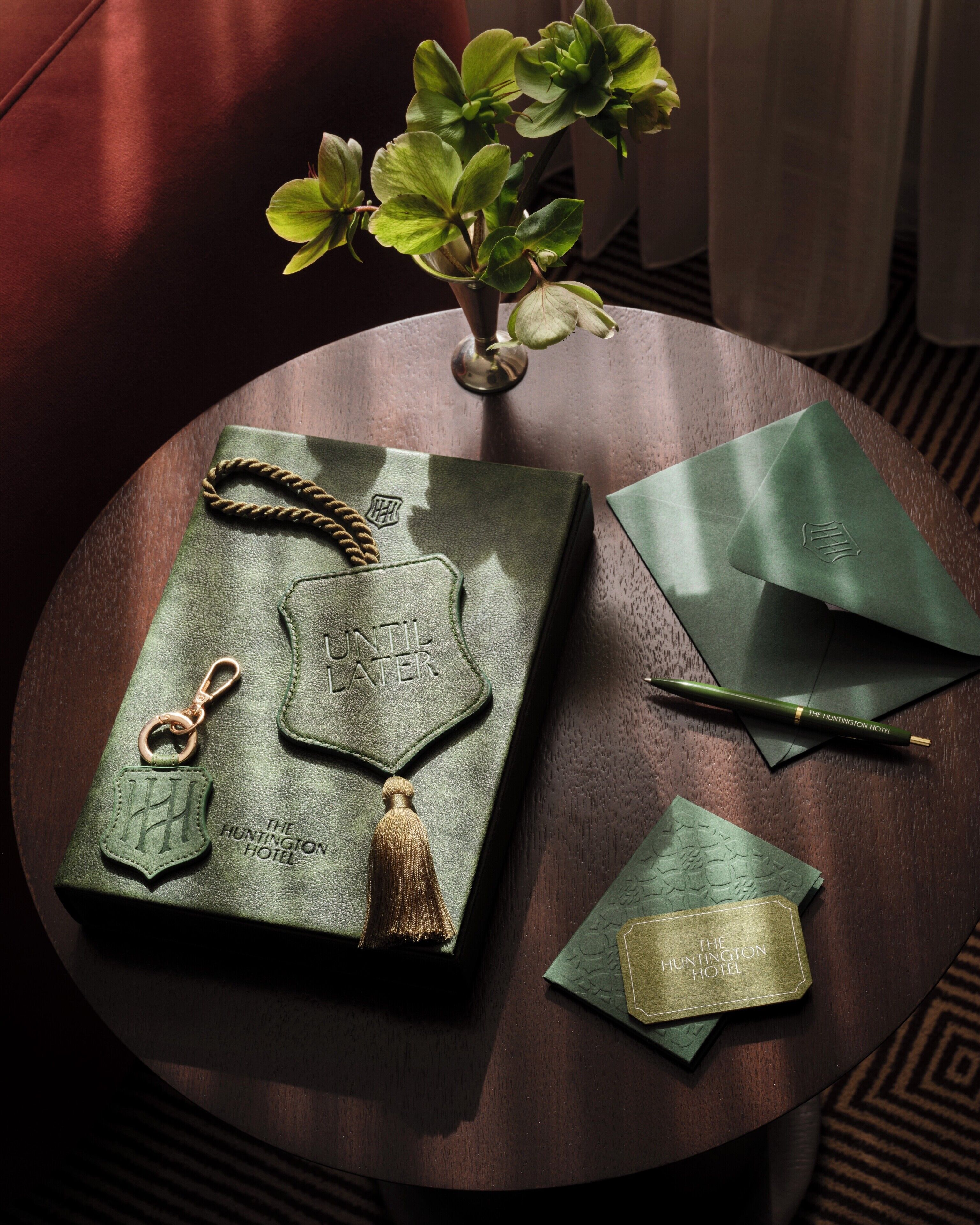 A leather-bound book with embossed text, a pen, a keychain, and a small potted plant on a round wooden table.