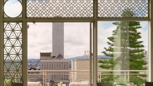 A balcony with a view of a tall building, a tree, and a table with chairs.