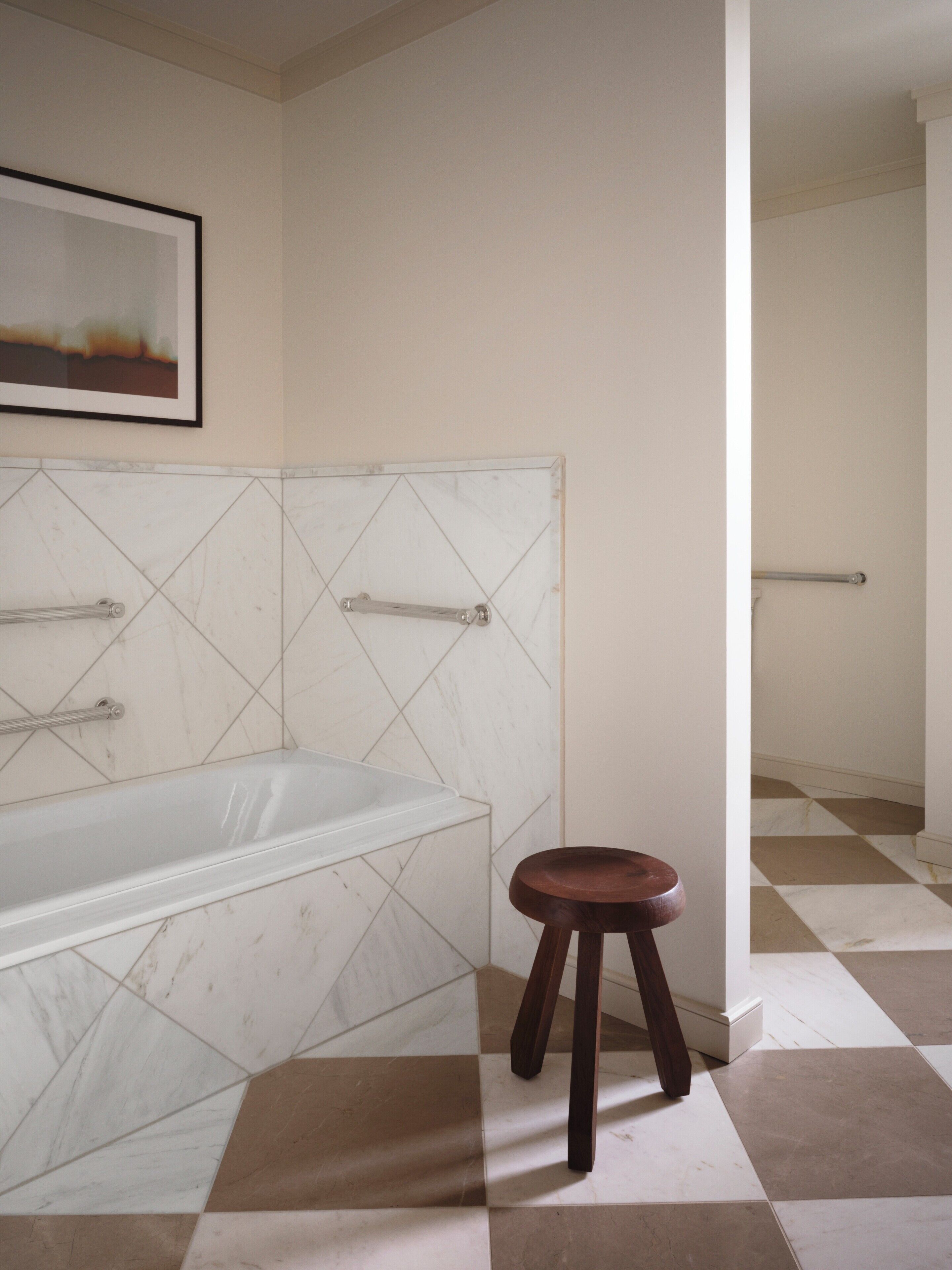 A bathroom with a bathtub, a wooden stool, and a handrail.