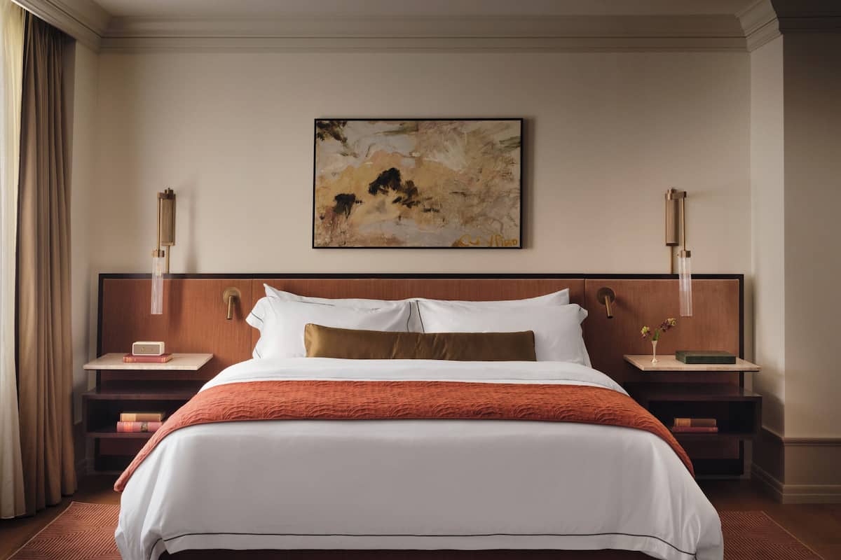Habitación de hotel con una cama grande, dos mesitas de noche, un cuadro en la pared y una alfombra estampada.