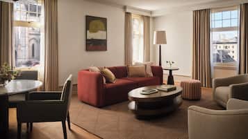A modern living room with a red sofa, a round coffee table, a lamp, and a view of buildings through large windows.