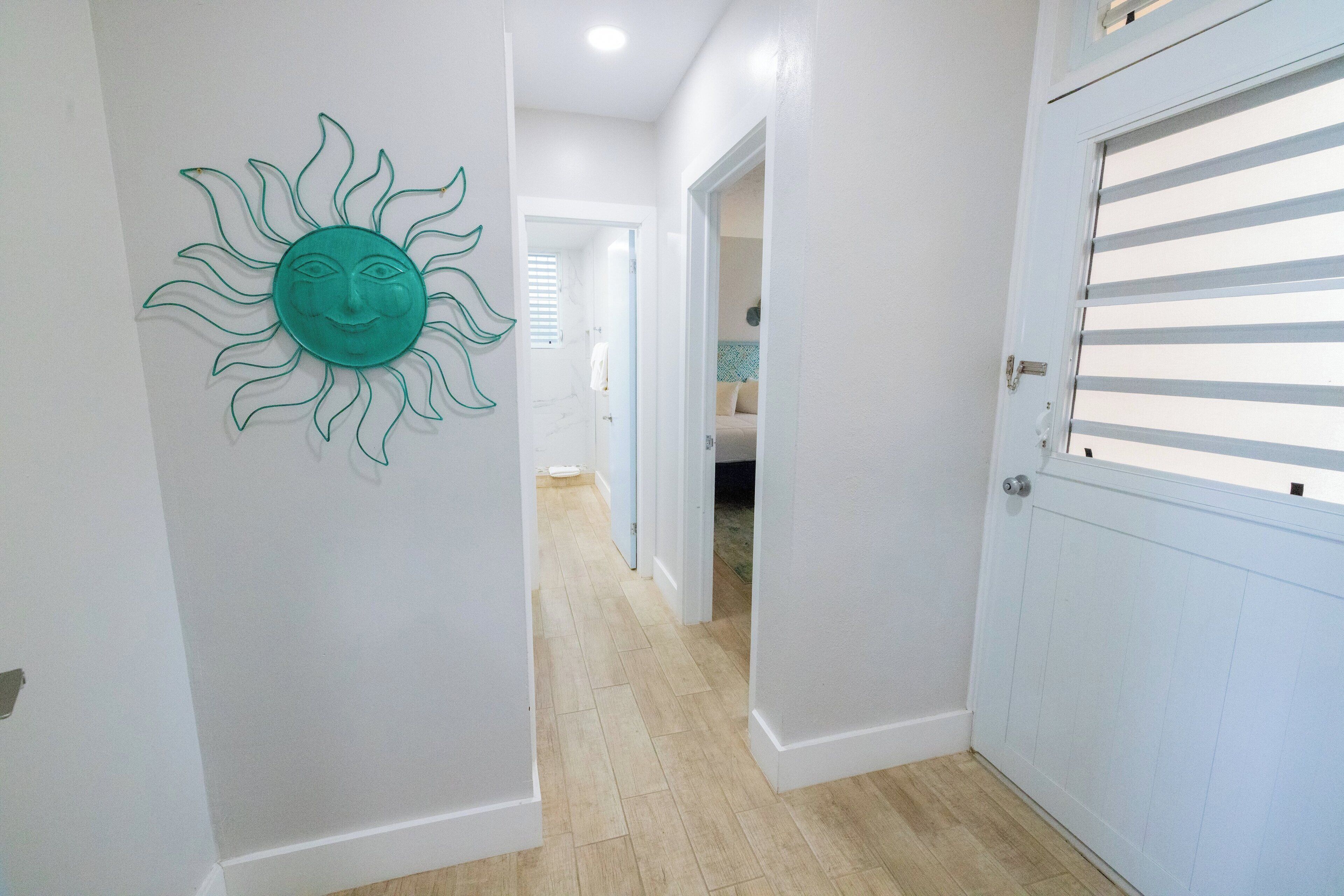 A hallway with a sun decoration, a door with horizontal blinds, and a light-colored floor.