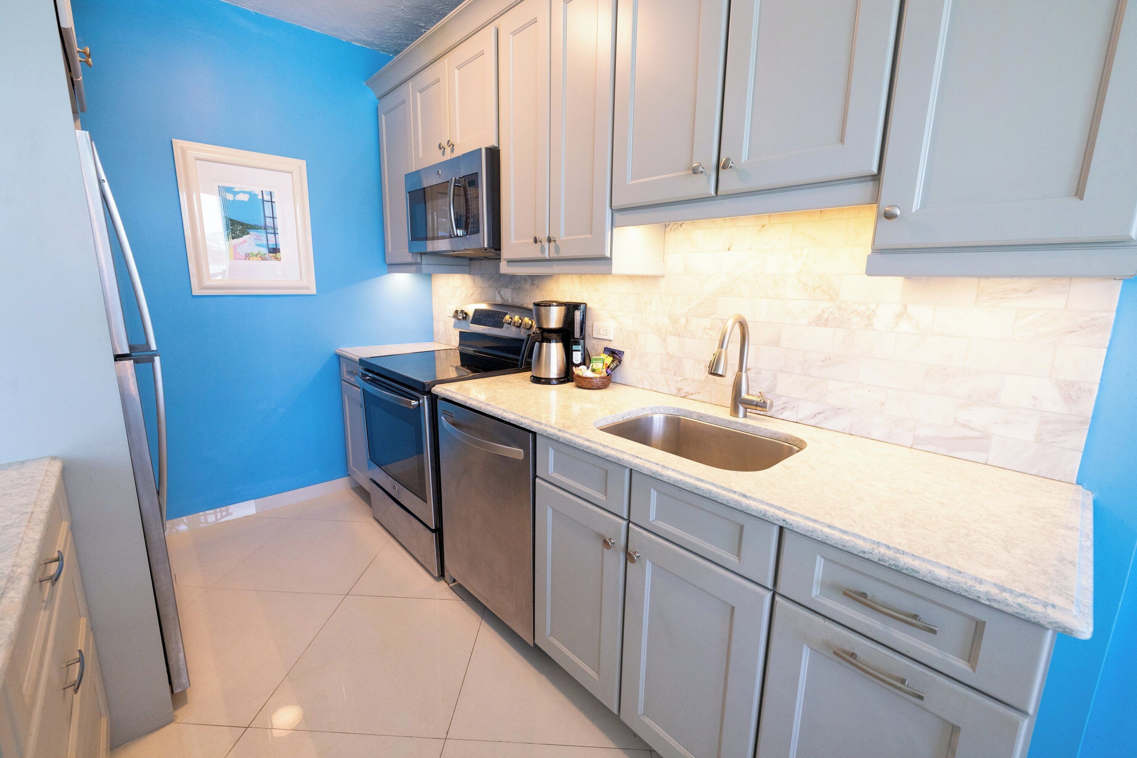 A kitchen with white cabinets, a stainless steel sink, a microwave, and a coffee maker.