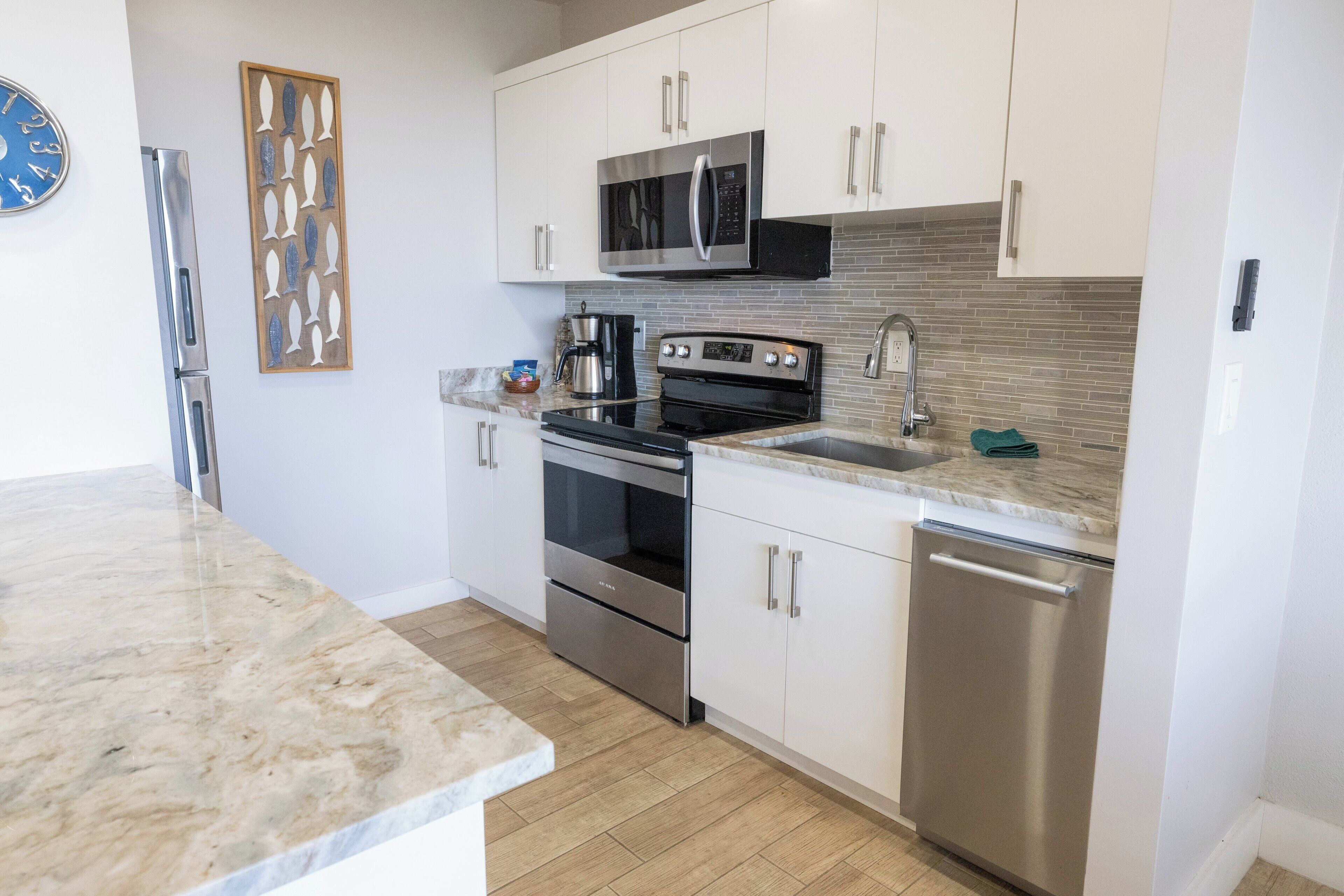 A modern kitchen with stainless steel appliances, white cabinets, and a tiled backsplash.