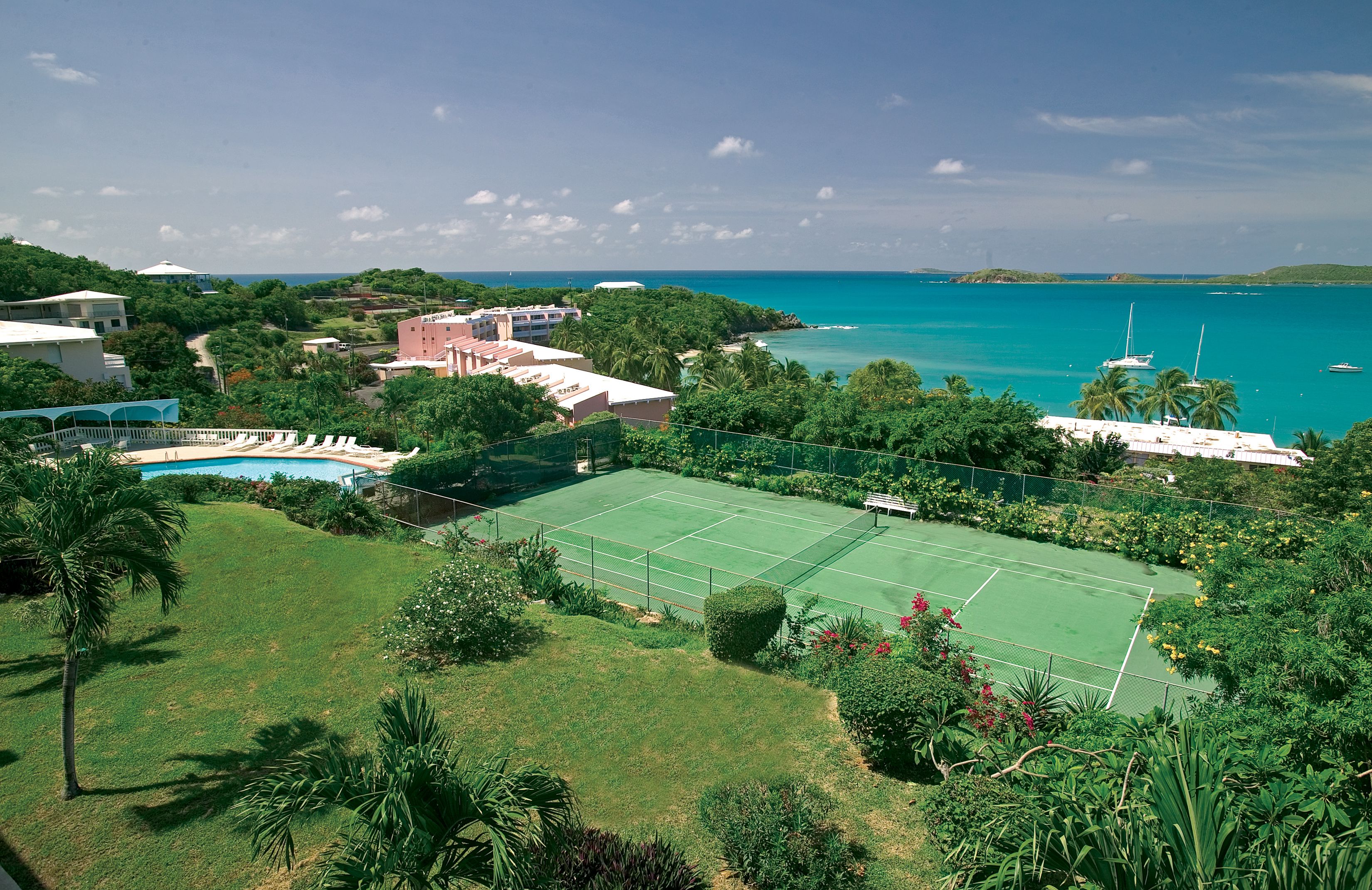 A tennis court surrounded by lush greenery and a view of the ocean.