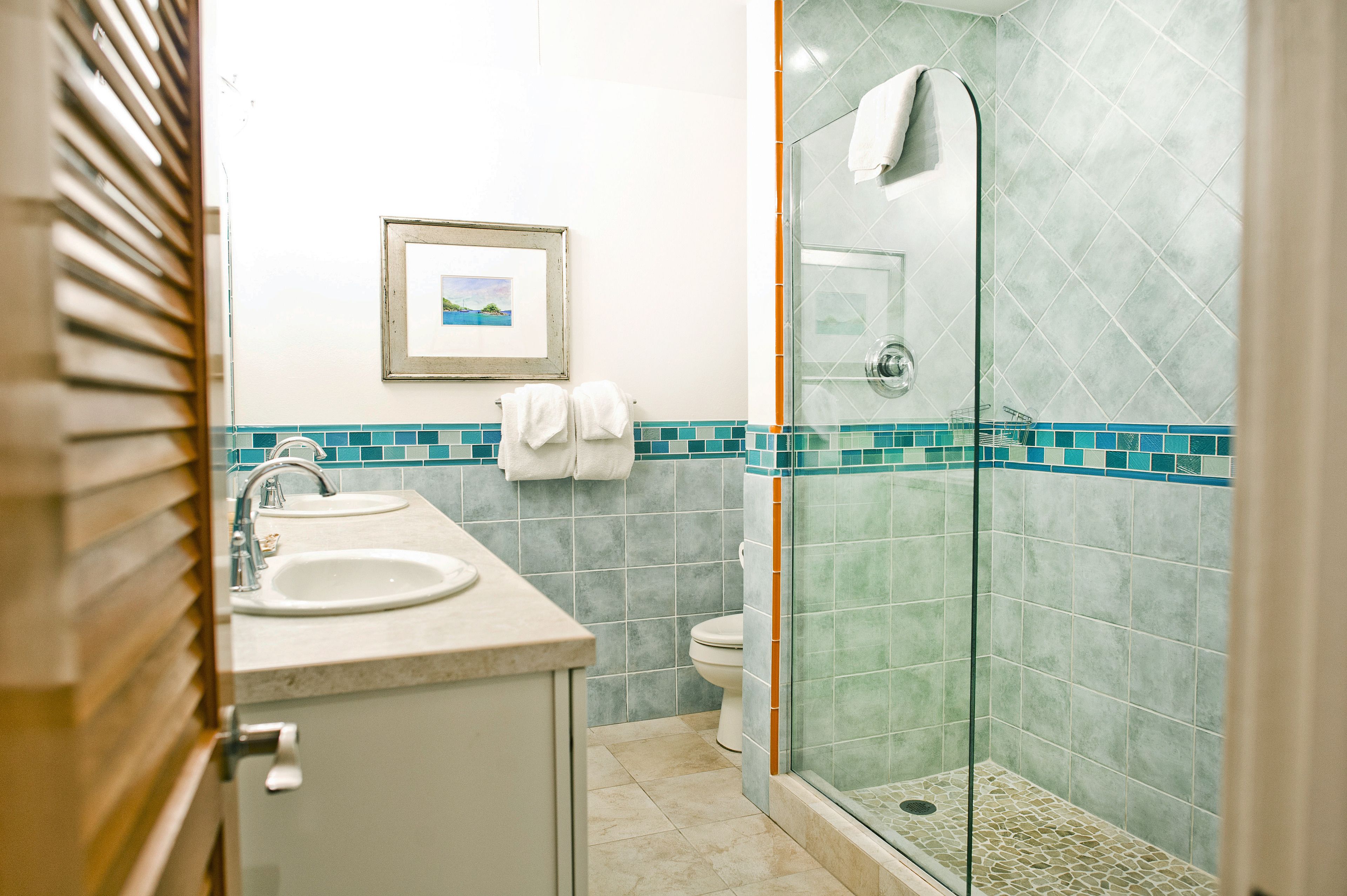 A bathroom with two sinks, a toilet, a glass shower enclosure, and a framed picture on the wall.