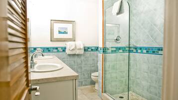 A bathroom with two sinks, a toilet, a glass shower enclosure, and a framed picture on the wall.