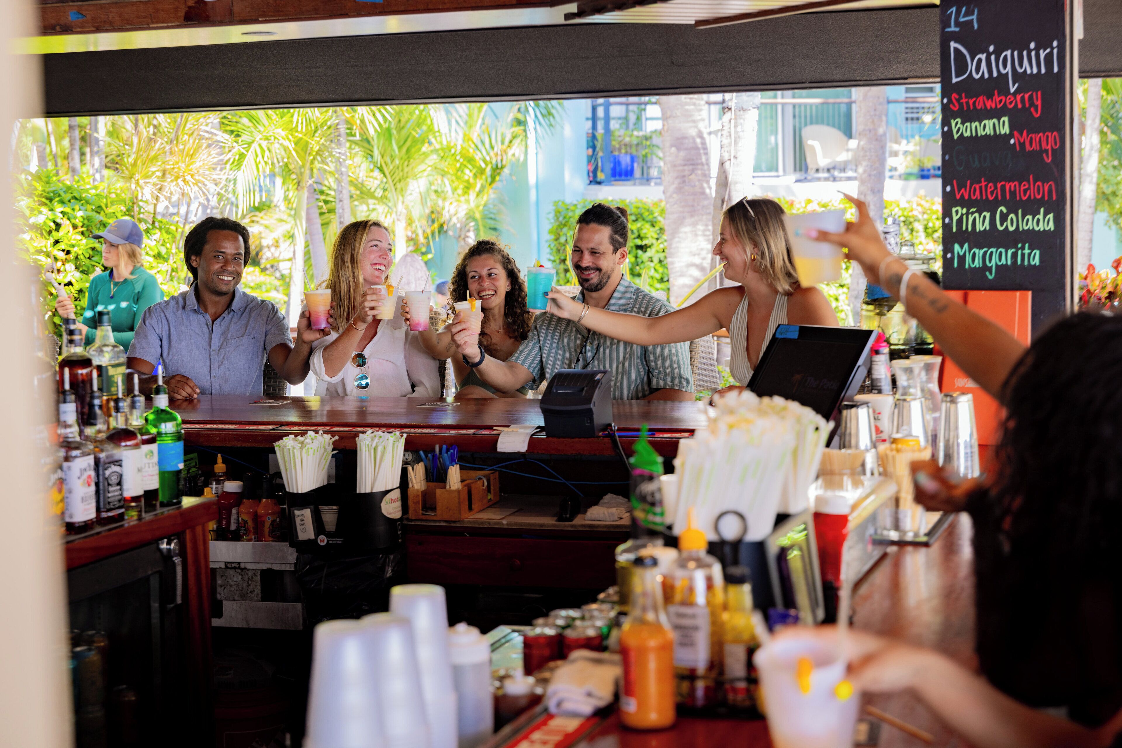 A group of people at a bar with a menu board listing drinks.