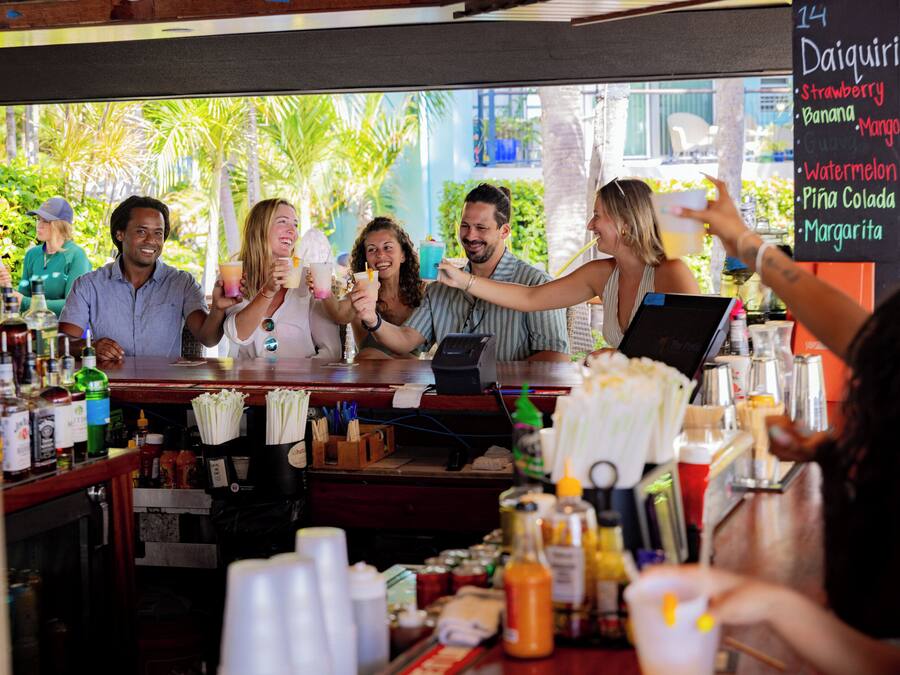 A group of people at a bar with a menu board listing drinks.