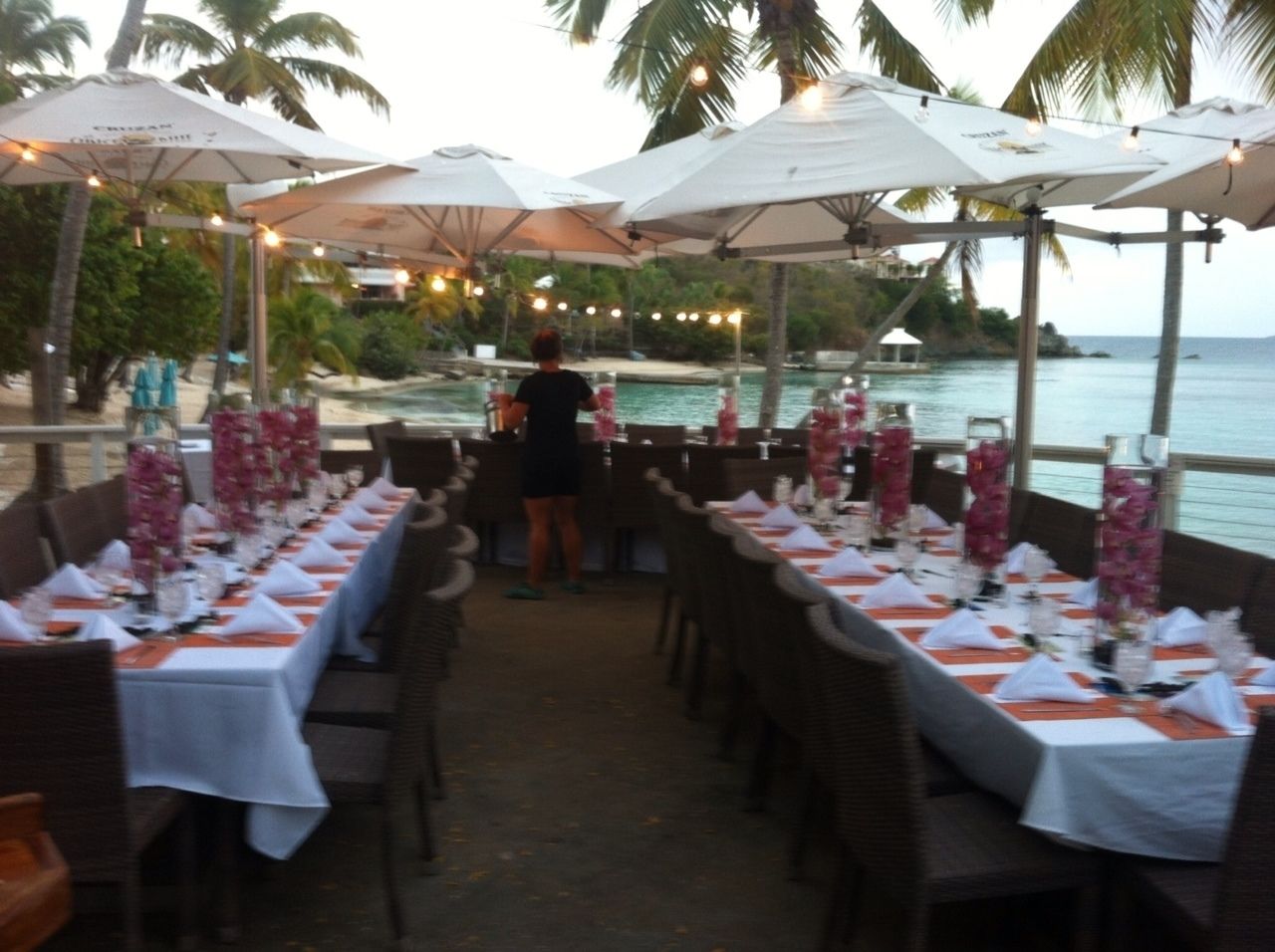 A restaurant with tables set for dining, outdoor umbrellas, and a view of the sea.