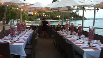 A restaurant with tables set for dining, outdoor umbrellas, and a view of the sea.