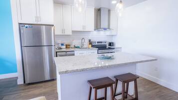 Una cocina moderna con armarios blancos, electrodomésticos de acero inoxidable, encimera de granito y dos taburetes de bar.